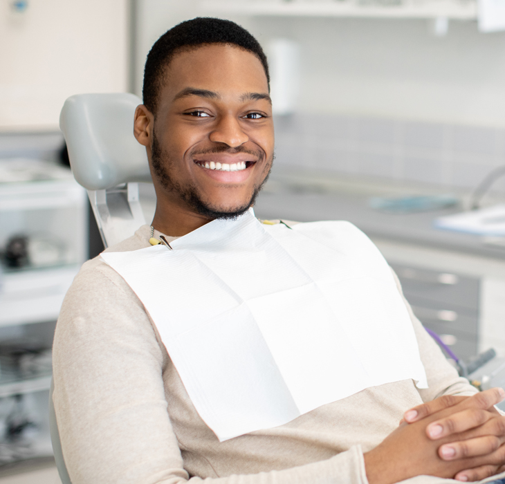 Smiling male patient in dental bib seated in modern dental office chair.
