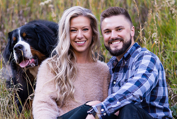 Smiling couple with dog posing outdoors in natural setting for dental practice portrait.