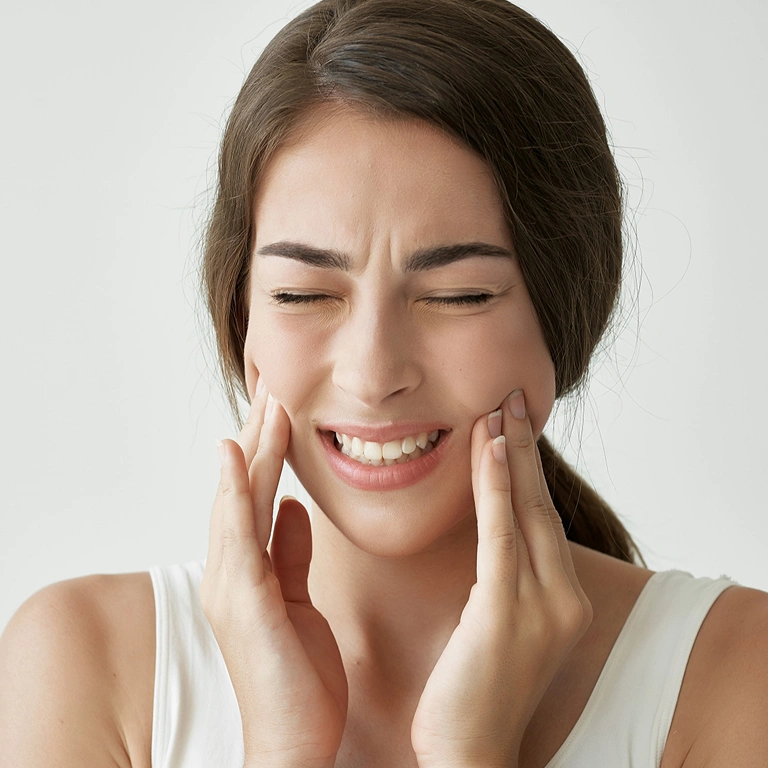 Woman holding cheeks with hands, smiling, displaying dental health against white background.