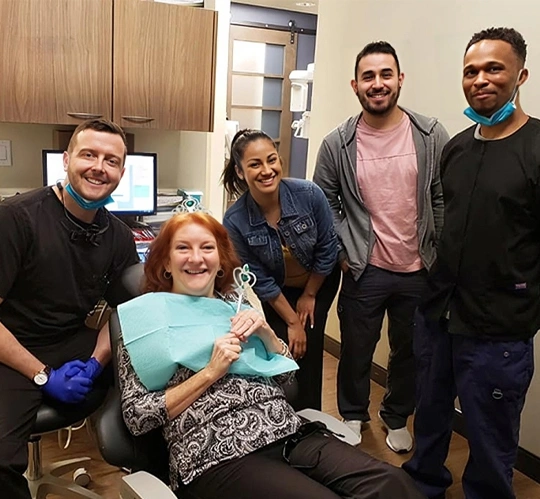 Dental team and patient smiling together in treatment room at Sierra Dental & Orthodontics clinic.