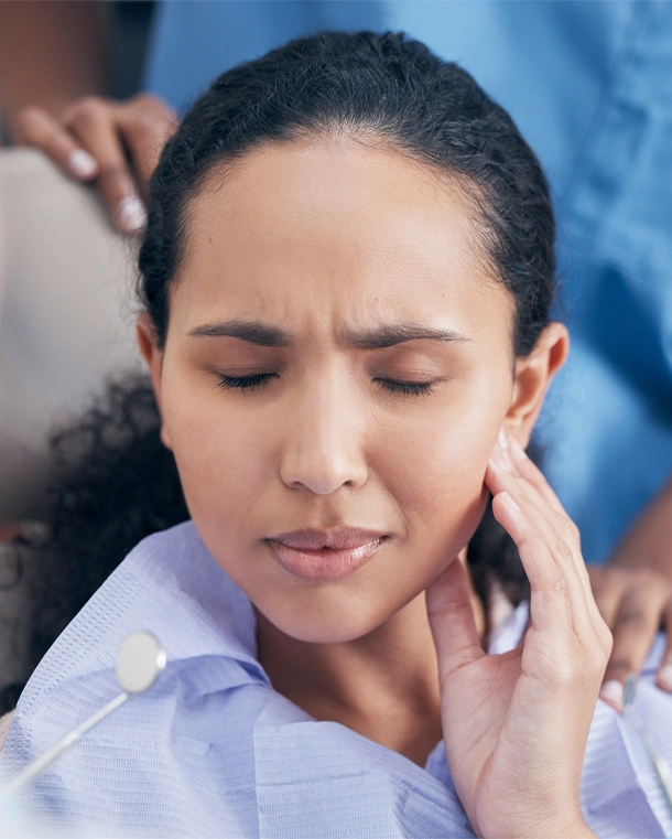 Woman holding jaw in pain against blue background, dental discomfort concept.