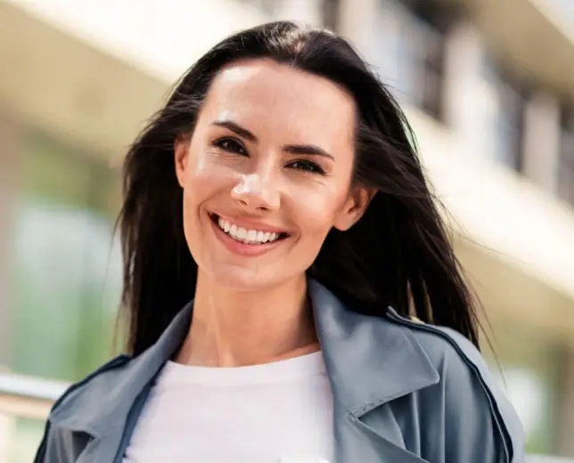 Smiling woman in casual blue jacket outdoors, professional headshot for dental practice.